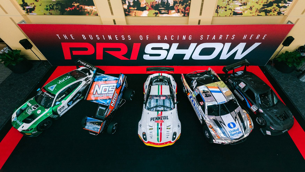 Line of race cars in front of PRI Show sign