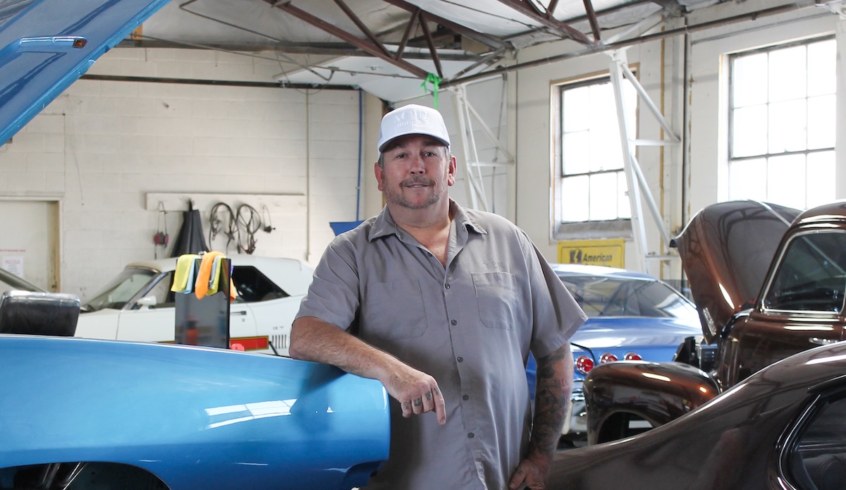 acme chop shop jack weaver poses in garage in front of cars