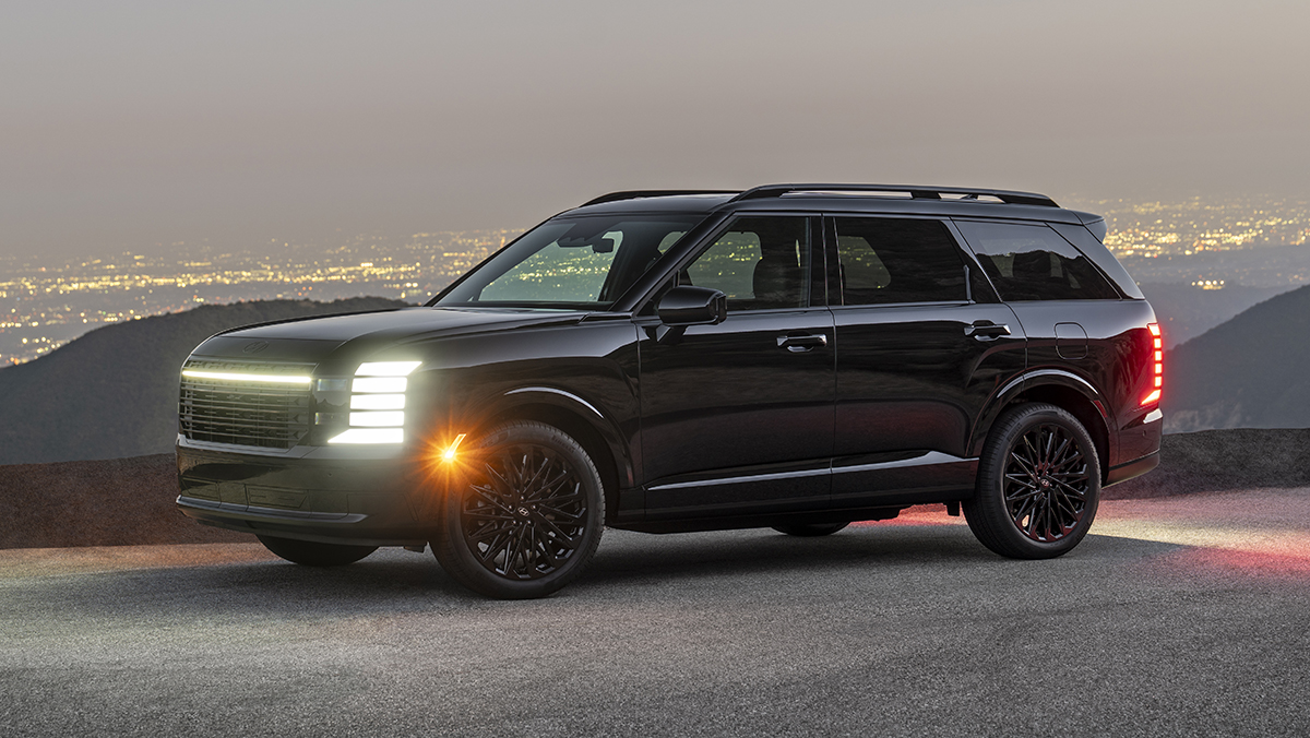 2027 Palisade Hybrid Calligraphy Black Ink Edition three-quarter front view with lights on at dusk