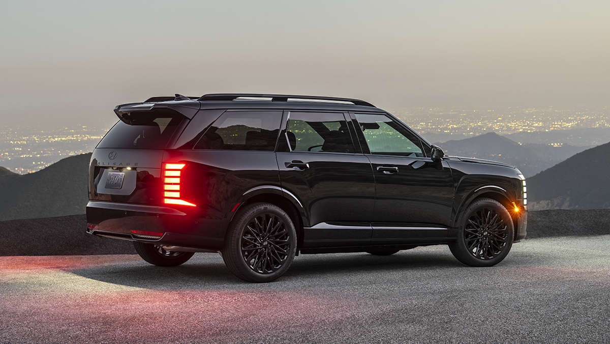 2027 Palisade Hybrid Calligraphy Black Ink Edition three-quarter rear view with lights on at dusk
