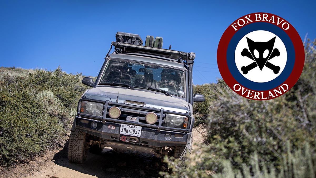 Defender on dirt trail with Fox Bravo Overland logo
