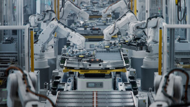 Row of White Robotic Arms at Automated Production Line at Bright Modern Factory. Electric Car Manufacturing Inside Automotive Smart Factory. Industrial Robot Arms Assemble Lithium-Ion EV Battery Pack