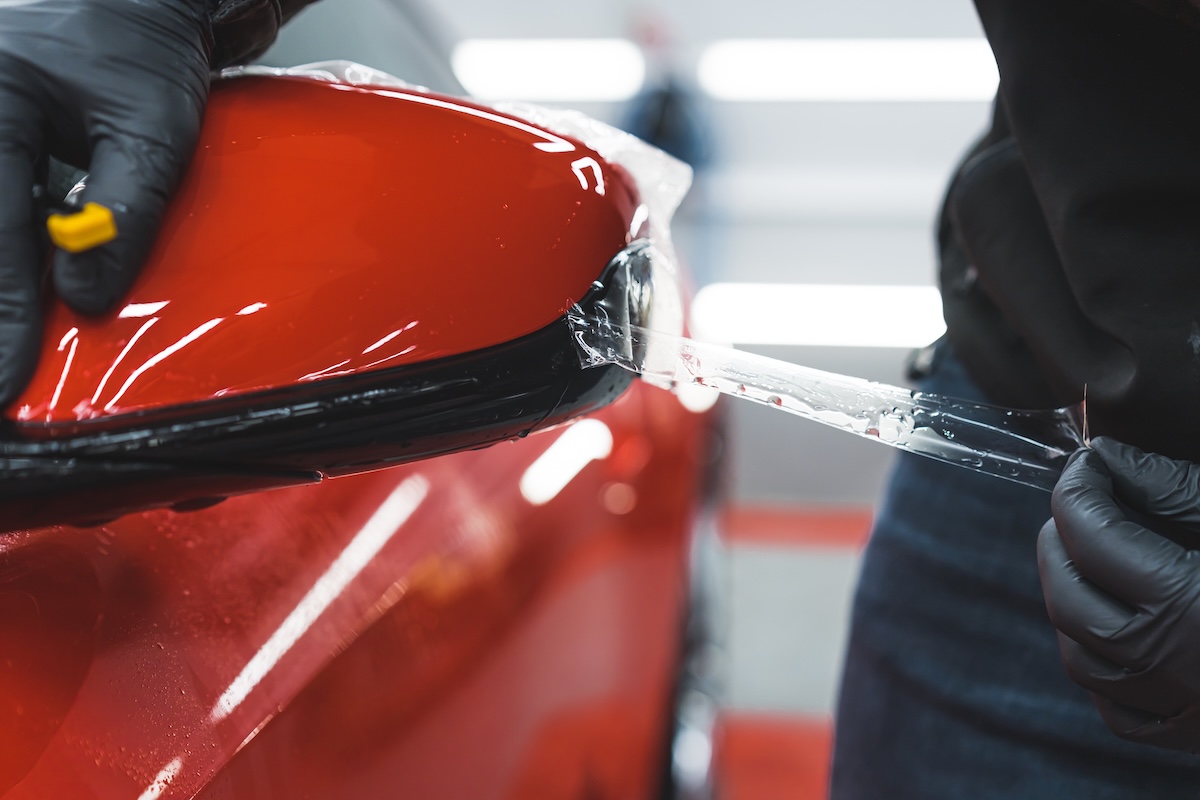 Lubrizol extreme closeup shot of professional car detailing expert applying or removing transparent foil from a red car. Blurred background.