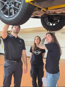 MINI Rebelle Rally team inspects front end of car on lift with team engineer