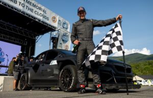 Subaru Motorsports Scott Speed at finish line with checkered flag and WRX: Midnight